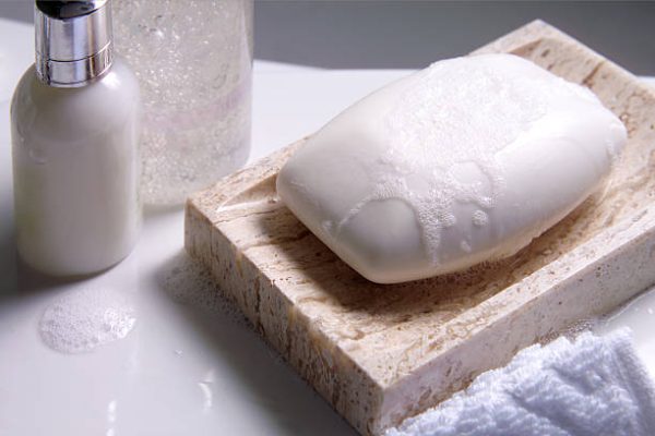 A soapdish with soap and other bath related items sits on the edge of a bathtub.